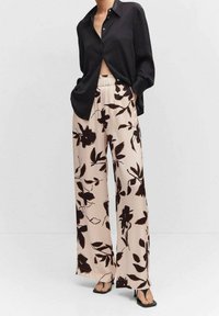 Chemise noire à manches longues avec fermeture à boutons, associée à un pantalon crème arborant un motif floral sombre et une coupe évasée.