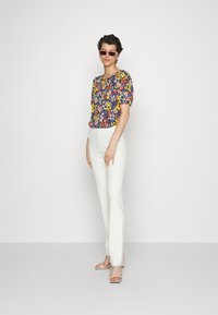 Top de padrão floral com mangas curtas em azul-marinho, combinado com calças brancas justas. Modelo usando óculos de sol rosas e sandálias de tiras.