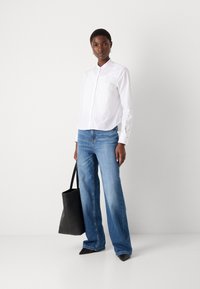 Witte blouse met een kraag, gecombineerd met lichtblauwe wijde jeans. Een zwarte leren tote bag en puntige zwarte hakken maken de look compleet.