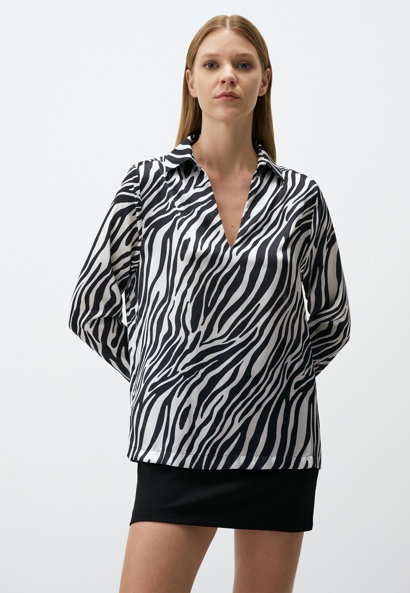 Blusa a strisce zebrate in bianco e nero con scollo a V, maniche lunghe e una consistenza liscia simile alla seta. Abbinata a una gonna nera.