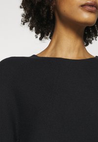 Pull en maille noire avec un large décolleté, tissu texturé et coupe décontractée. Orné de coutures discrètes et d'un ourlet courbé.