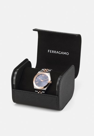 Ferragamo watch in a black box. Octagonal rose gold and silver case, blue dial with Roman numerals, and a patterned band.