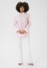 Long-sleeve, button-up shirt featuring pink and yellow vertical stripes, crafted from lightweight fabric. Paired with white flared pants.