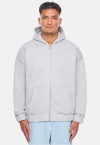 Helle graue Zip-Hoodie aus weichem Stoff, mit einer Kängurutasche, gesticktem Logo auf der Brust und verstellbarem Kordelzug an der Kapuze.
