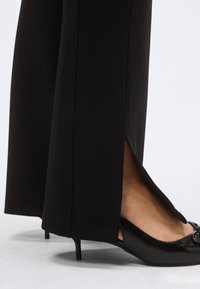 Mustad püksid külgmise lõhikuga, valmistatud siledast kangast; kombineeritud mustade teravate ninadega kontsakingadega, millel on dekoratiivne aksent.