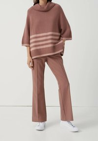 Ylimitoitettu vaaleanpunainen neulottu poncho, jossa on ribbineulottu kaulus ja vaakasuorat raidat. Yhdistetty vaaleanpunaisiin leveälahkeisiin housuihin ja valkoisiin lenkkareihin.