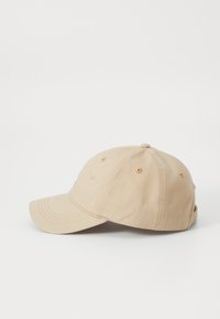 Beige baseball cap med en bøjet skygge. Fremstillet af bomuld, med seks ventilationshuller og et justerbart rem bagpå.