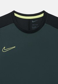 Tume roheline spordisärk mustade õlaaktsentide ja kollase kaelusega; väikese kollase Nike logoga ning niiskust imava materjaliga.