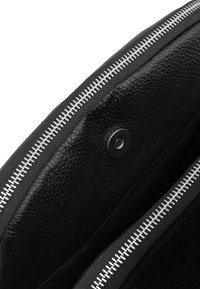 Interior de un bolso de cuero negro texturizado que muestra un botón de presión magnético plateado y una cremallera metálica plateada parcialmente abierta.