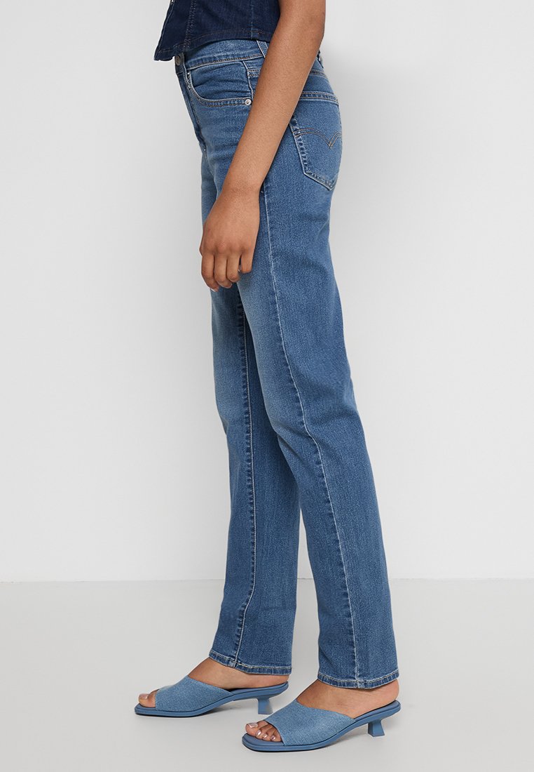 Jeans in denim blu con design a gamba dritta, cinque tasche e leggere sfumature. Abbinati a sandali scivolati blu chiaro.