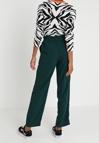 Pantalon large vert avec une taille élastique, associé à un pull à motifs zèbre noir et blanc, doté d'un col rond et de manches longues.
