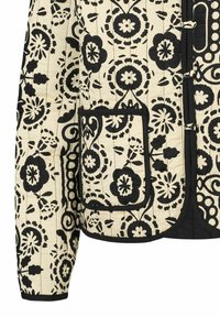 Giacca trapuntata nera e crema con motivi floreali, una tasca e rifiniture a contrasto. Chiusura frontale con anelli e toggle.