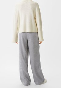 Krämfärgad stickad tröja med kort fåll och ribbade detaljer, kombinerad med grå, vertikalt randiga byxor med vida ben. Mjuk textur överallt.