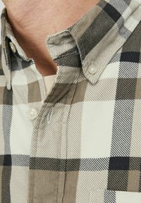 Camisa de botones con un patrón de cuadros en tonos de beige, marrón y negro. Hecha de tela texturada con un collar estándar y botones.