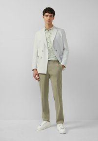 Hellgrauer doppelt geknöpfter Blazer, Blumenhemd, olivgrüne Hose und weiße Sneakers. Strukturiertes Material, taillierte Passform, minimalistischesDesign.