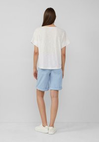 Witte top met korte mouwen gecombineerd met lichtblauwe opgerolde shorts. Minimalistisch ontwerp met een ontspannen pasvorm, aangevuld met witte sneakers.