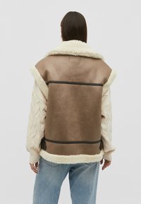 Hnědá umělá kožená bunda s krémovým střihem, pletenými béžovými rukávy a zipovým spodním lemem, zdobená horizontálními švy.