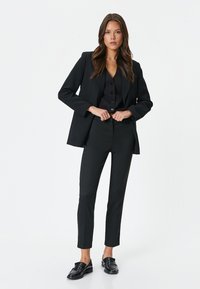 Czarny elegancki garnitur składający się z marynarki, kamizelki z guzikami i slim-fit spodni. W połączeniu z błyszczącymi czarnymi loafersami. Gładka faktura tkaniny.