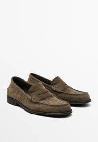 Mocassins en daim marron au design de type moccasin, avec des détails cousus et une semelle en caoutchouc noir slim. Talon plat et orteil arrondi.