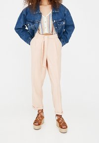 Lichtroze high-waisted broek met een strikceintuur, gecombineerd met een gestreepte cropped top en een spijkerjacket. Bruine sandaalplatforms.