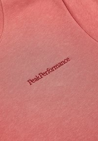 Różowa tkanina bawełniana z domieszką, o gładkiej fakturze, z haftowanym logo "PeakPerformance" w nieco ciemniejszym odcieniu różu.