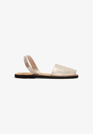 Sandalia plana beige de punta abierta con tira trasera y suela negra, diseño minimalista para uso casual.