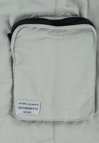 Pochette en tissu gris clair avec une fermeture éclair noire et une étiquette blanche indiquant les coordonnées et le texte « LEVI STRAUSS & CO EST. 1873 ».