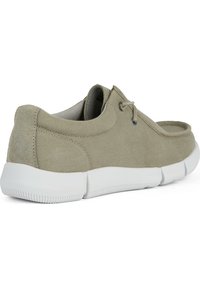Chaussures décontractées en suède beige avec un profil bas, semelle en caoutchouc blanche et design minimaliste. Présente des coutures discrètes et un système de laçage.