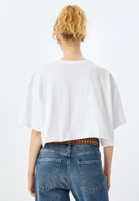 Hvid cropped T-shirt med en afslappet pasform, korte ærmer og rund halsudskæring. Kombineret med højtaljede blå denimjeans og et brunt spænde med nitter.