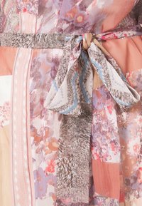 Meer kleurige jurk met bloemachtige en geometrische patronen, met een textuurrijke tailleafwerking met riem. Voornamelijk in tinten roze, blauw en beige.
