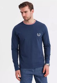 Navy long-sleeve shirt with a crew neckline, featuring red and white striped accents. Includes a small embroidered logo on the chest.