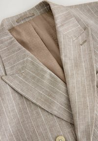 Blazer beige con righe bianche, tessuto testurizzato, revers a punta e fodera a motivo color sabbia. Chiusura con un solo bottone sul davanti.