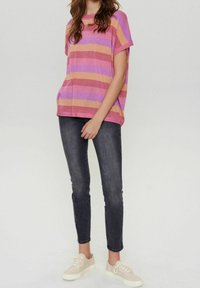 Top de manga corta, de corte relajado con rayas horizontales en rosa, naranja y púrpura; combinado con jeans oscuros ajustados y zapatillas ligeras.