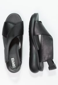 Sandali neri in pelle con design a fasce incrociate, soletta imbottita, suola in gomma resistente e linguetta per una facile indossabilità.