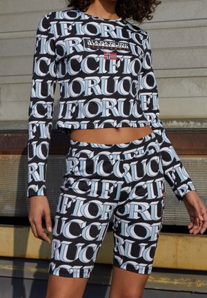 Persoon draagt een bijpassend zwart-wit langemouwen top en korte broek met een groot herhalend tekstpatroon en een Napapijri-logo met een kleine vlag.