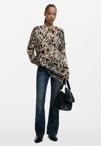 Djurmönstertröja i beige och svart, avslappnad passform med långa ärmar; matchad med vida blå jeans och en svart handväska.