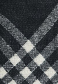 Tessuto a scacchi in bianco e nero con una trama testurizzata, caratterizzato da motivi a diamante e quadrati alternati. I bordi sono puliti e ben definiti.