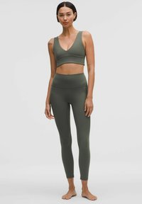 Olíva zöld sportmelltartó és leggings szett rugalmas anyagból, mély V-nyakú dizájnnal és magas derékú leggings-szel, lapos varrásokkal.