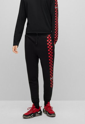 Czarne dresy z czerwonym wzorem w kratkę wzdłuż boku, związywanie w talii i detalem logo. Noszone z czerwono-czarnymi sneakersami.