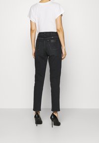 Svarta denimjeans med smal passform, hög midja och klassiska bakfickor, parat med svarta högklackade skor och en vit t-shirt.