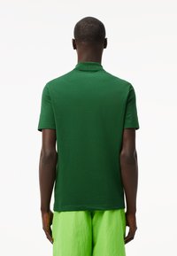 Polo verde con cuello y mangas cortas, hecho de tela de punto. La parte trasera presenta una textura suave con un diseño simple.