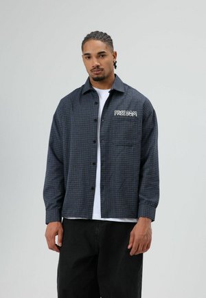 Geruite marineblauwe overhemdjack met zwarte accenten en een voorvak met de tekst "FREEDOM". Heeft een ontspannen pasvorm en knoopsluiting.