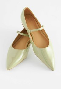 Grüne Lackleder-Ballerinas mit spitzen Zehen, ausgestattet mit einem dünnen Knöchelriemen und einem glatten Innenfutter. Keine sichtbaren Muster oder Beschläge.