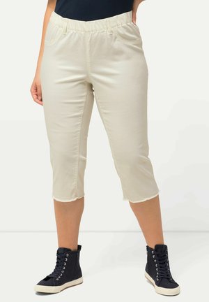 Pantalones cortos de color crema con cintura elástica, que cuentan con bolsillos laterales y dobladillos sin rematar, combinados con zapatillas altas navy.
