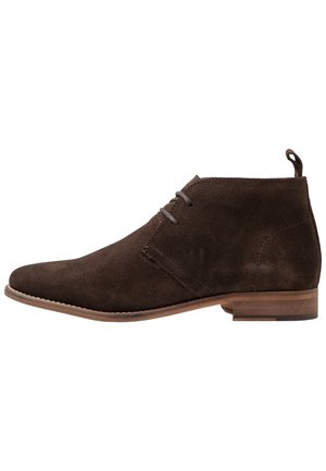 Brune ruskinds ankelstøvler med en slank profil, snøredesign og en lille hæl. Har en struktureret overflade og en trækflap bagpå.