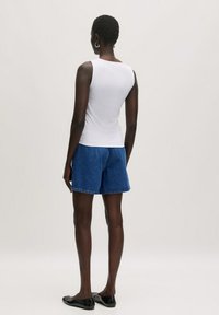 Weißes ärmelloses Oberteil, blaue Denim-Shorts, schwarze Ballerinas. Glattes Material, lässige Passform, Shorts bis zur Mitte des Oberschenkels mit umgeschlagenem Saum, einfaches Design.