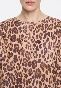 Animal print top featuring a tan background with dark brown leopard spots, round neckline, and smooth texture.
