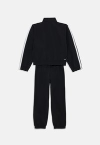 Tuta nera composta da una giacca con zip e strisce bianche sui lati e pantaloni coordinati con polsini elastici. Tessuto morbido con design minimalista.
