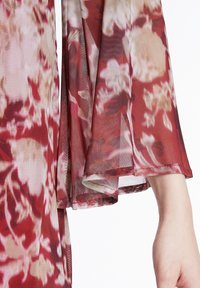 Blumenmuster-Kleidungsstück in Rottönen und Creme. Leichter Stoff mit weicher Textur, mit fließenden Ärmeln und einem detaillierten Saum.