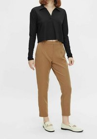 Czarna prążkowana koszulka polo z długim rękawem i kołnierzykiem, zestawiona ze zwężanymi brązowymi spodniami i białymi mokasynami ze złotymi akcentami.